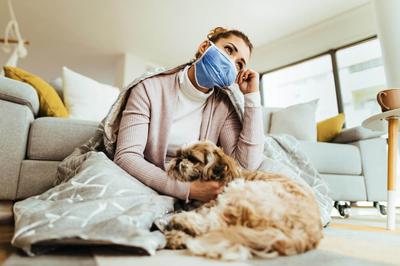 A woman thinking about dog coughing while wearing protective face mask with her dog at home